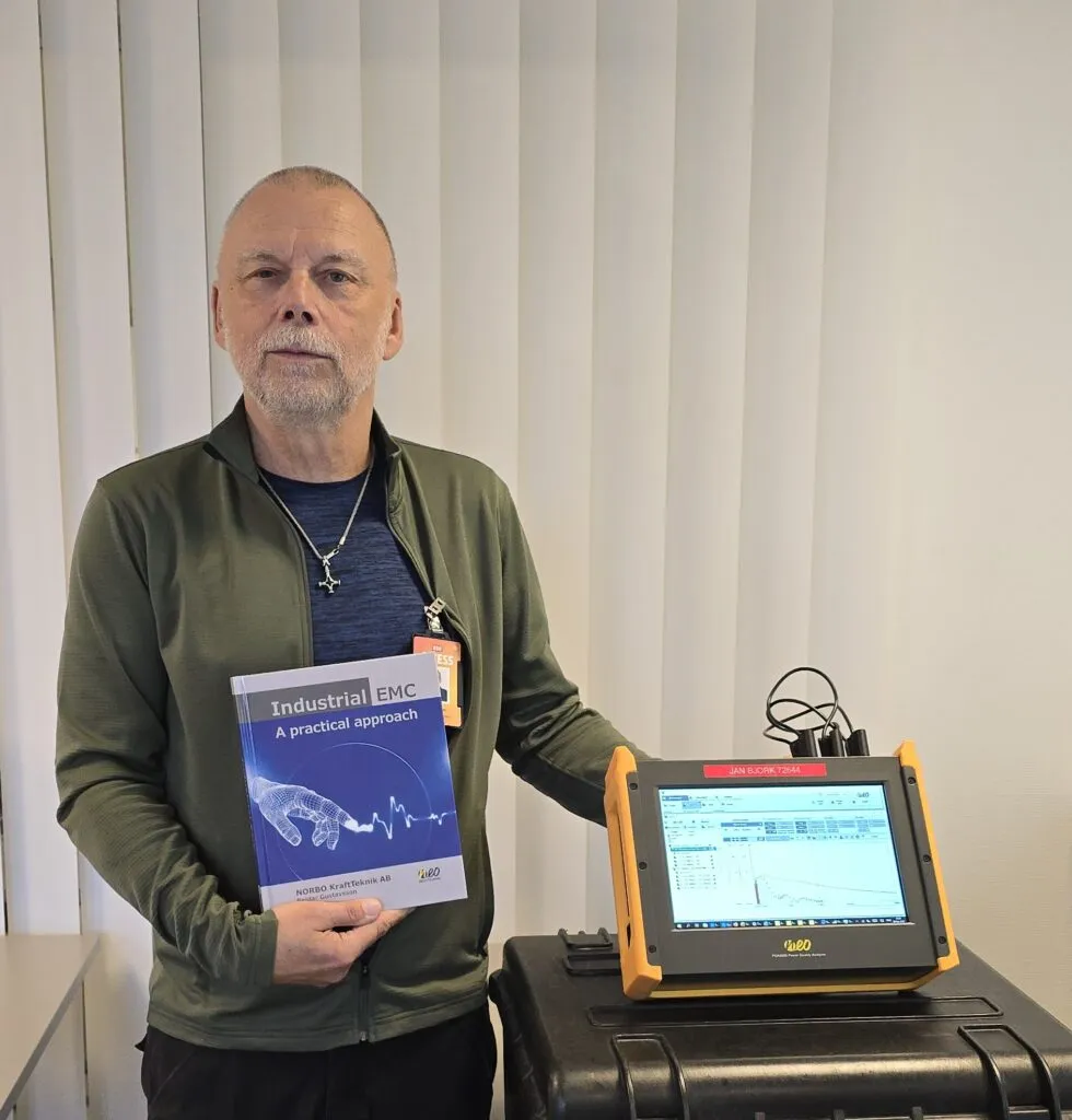 Reidar Gustavsson tenant son livre Industrial EMC à côté d’un analyseur de qualité réseau PQA8000 de NEO Messtechnik